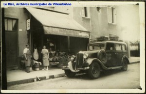 Devanture de l'épicerie rue du 4-Août avec le personnel et l'automobile en premier plan. Carte postale. [cote 2Fi66]